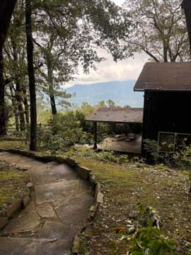 a stone pathway bends near a cabin with a eastern usa mountain overlook